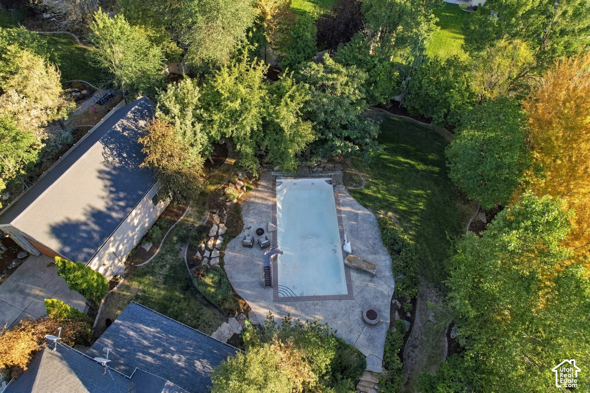 Outdoor swimming pool with a surrounding hardscape patio, an adjacent detached structure, and mature landscaping