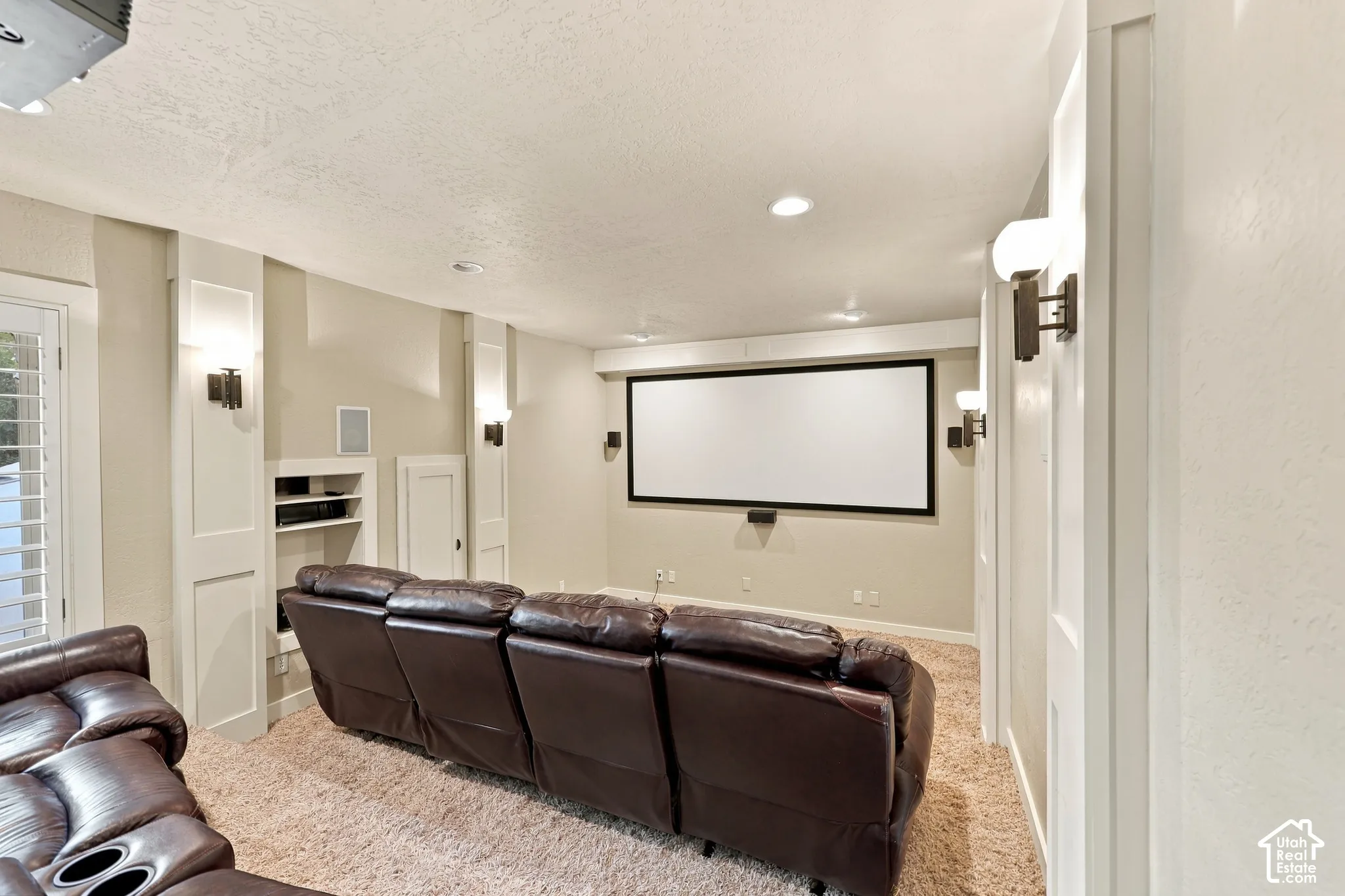 Dedicated media room featuring a large projection screen, built-in media shelving, sconce lighting, and recessed ceiling lighting