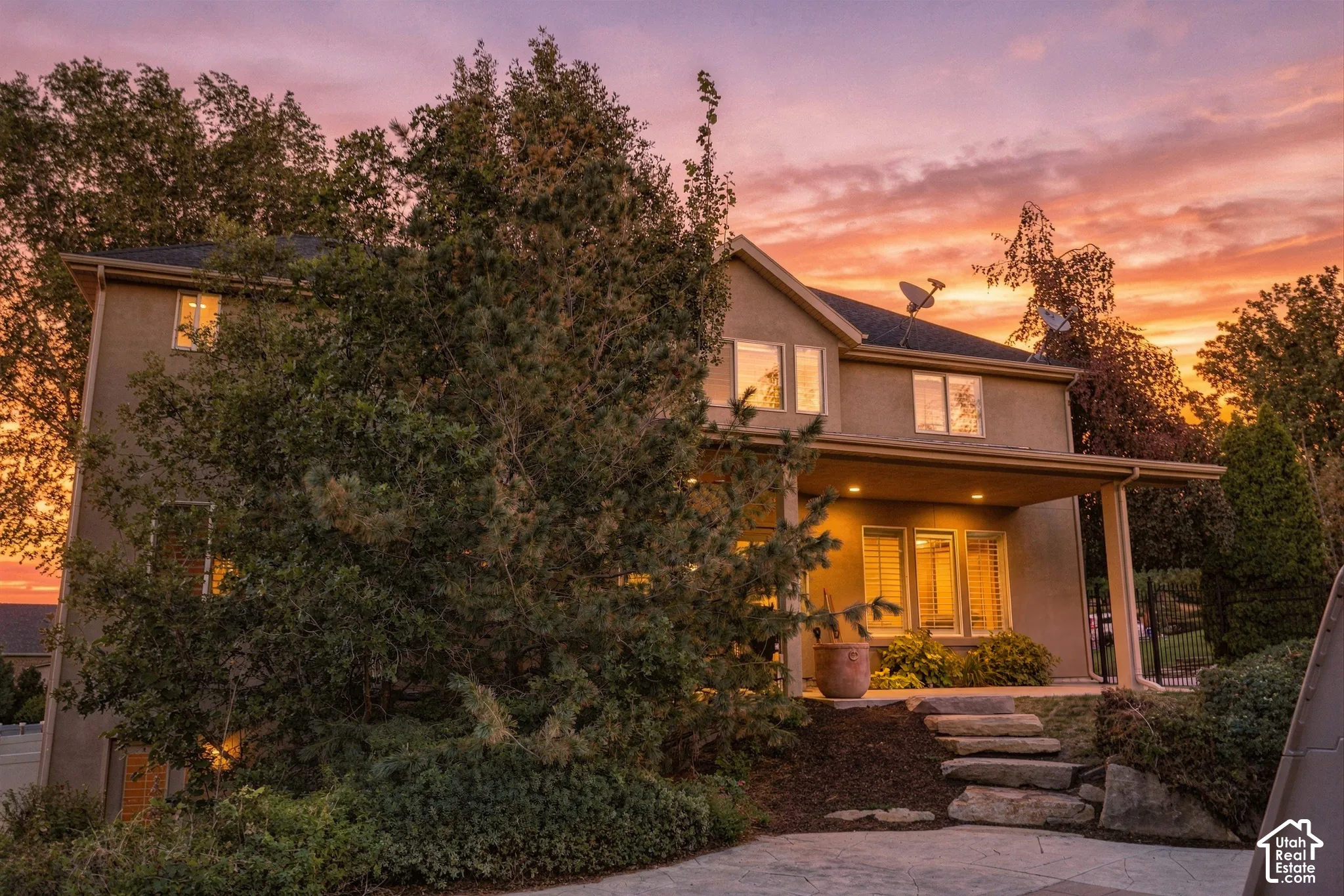 Stucco exterior with multiple windows, covered patio, recessed lighting, and stone steps