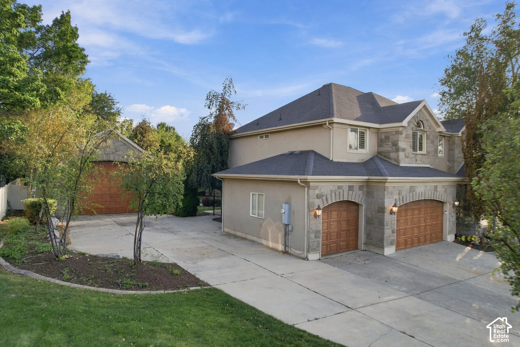 Stucco exterior with stone accents, arched garage doors, a multi-car driveway, and mature landscaping