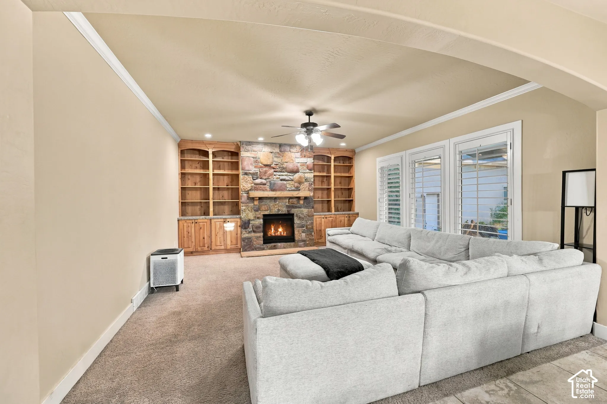 Stone-clad fireplace with a wood mantel, built-in shelving, wood-finish cabinetry, and recessed lighting