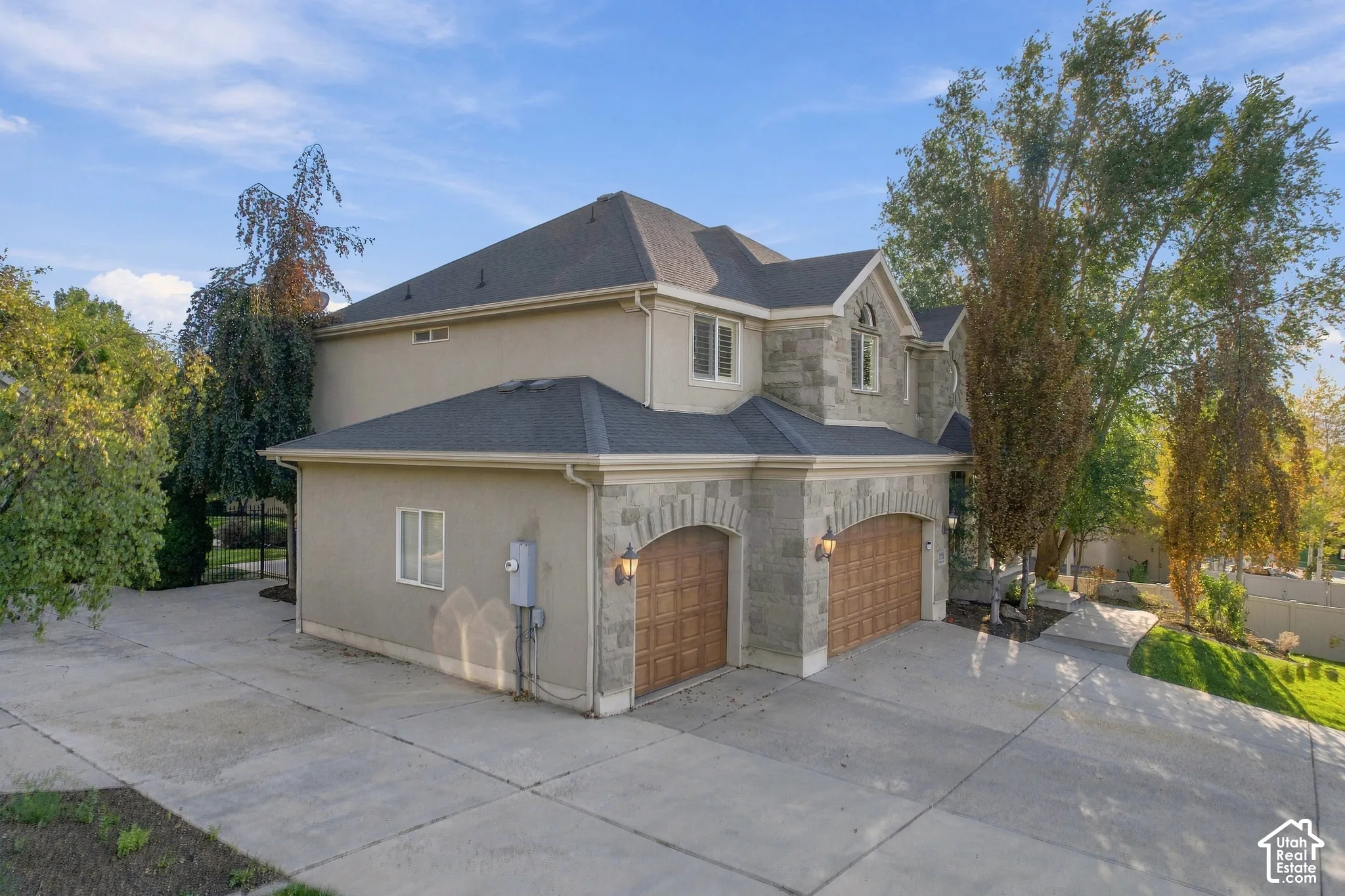Stucco exterior with stone accents, arched garage door openings, decorative garage doors, and a paved driveway