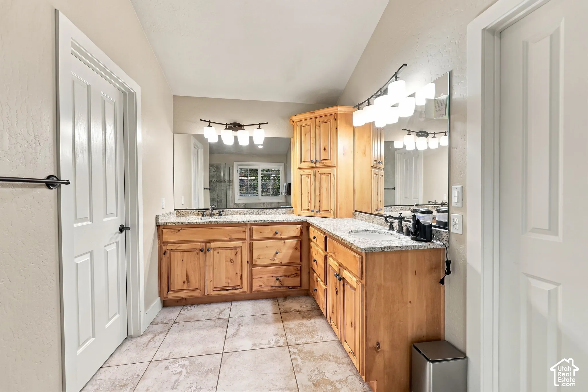 Dual vanity with light wood cabinetry, stone countertops, and integrated sinks