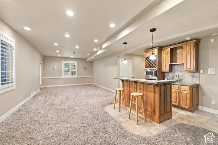 Spacious room featuring plush carpet, recessed lighting, white louvered window treatments, and a built-in wet bar with wood cabinetry and a granite countertop