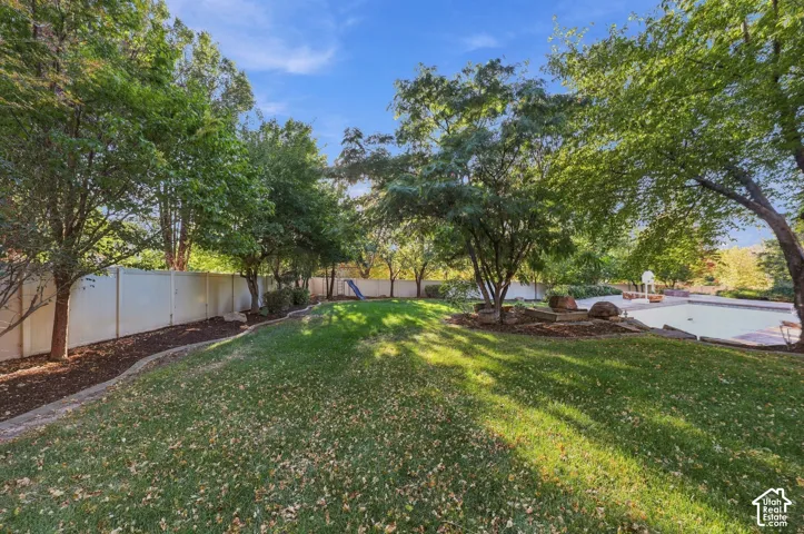 Expansive lawn featuring mature trees, a privacy fence, and a swimming pool with surrounding hardscaping