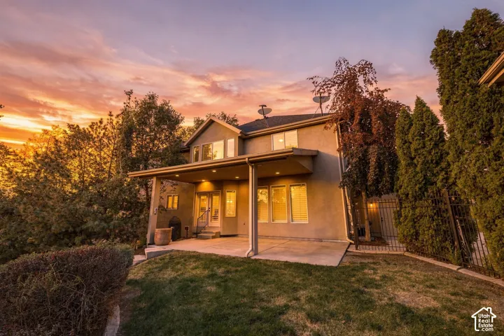 Stucco exterior with a covered patio, concrete hardscaping, and a landscaped yard featuring mature trees and shrubs