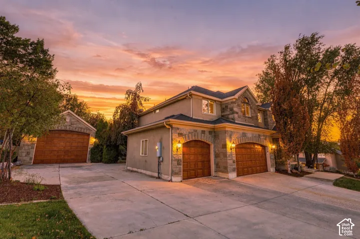 Stone and stucco exterior with multiple gables, arched wood-finish garage doors, exterior lighting fixtures, and an additional detached garage structure