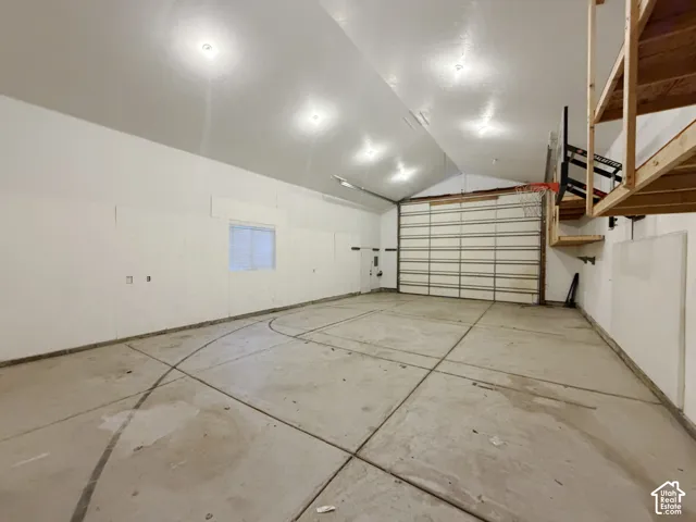 Spacious garage featuring polished concrete flooring, recessed LED lighting throughout, overhead storage shelving, and a single-panel garage door with window insert