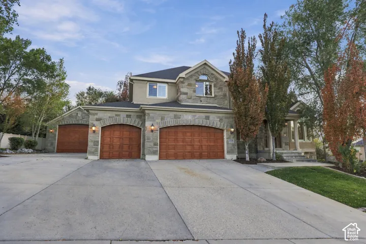 Stone facade architecture with arched garage doors, concrete driveway, and mature landscaping