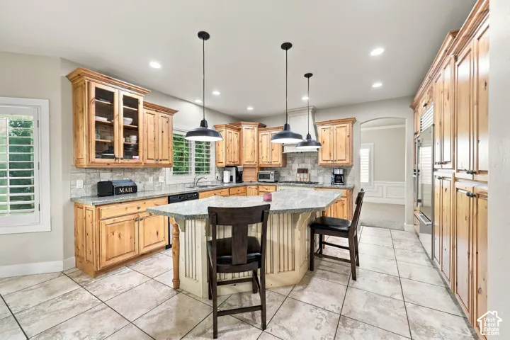 Custom wood cabinetry, stone countertops, integrated appliances, and a central island with pendant lighting