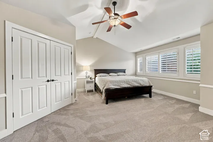 Vaulted ceiling with a ceiling fan, light-toned carpeting, white paneled bifold doors, window shutters, and wainscoting