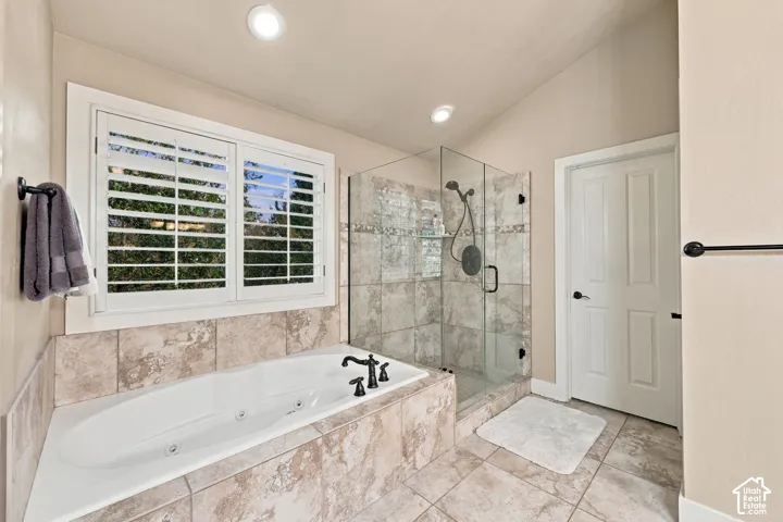 Recessed lighting illuminates a built-in jetted tub with tile surround, a glass-enclosed shower with tile walls, and a window featuring white plantation shutters