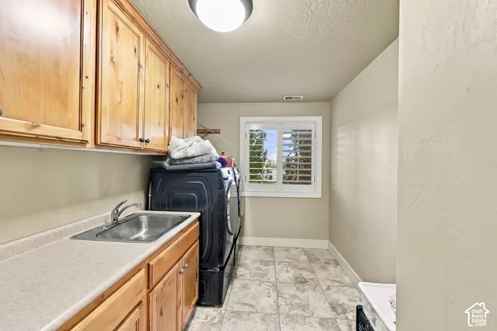 Laundry area featuring a utility sink, light wood-finish cabinetry, and a window with white shutters