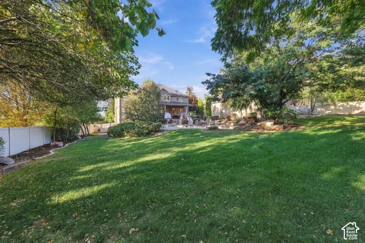 Expansive green lawn with mature trees and a white privacy fence