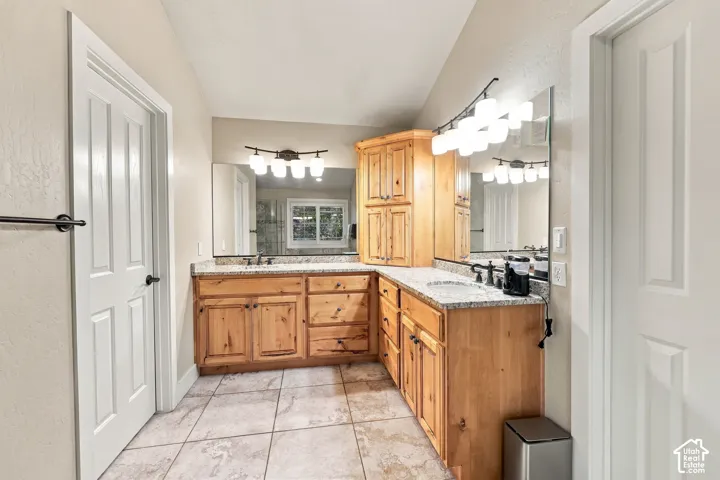 Dual vanity with light wood cabinetry, stone countertops, and integrated sinks