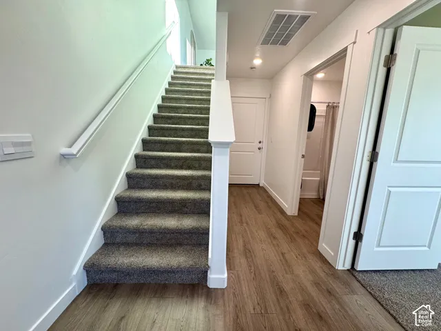 Carpeted staircase with white railing, wood-finish flooring, recessed lighting, and white interior doors