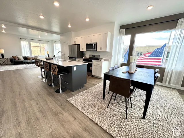 Open-concept living space featuring wood-finish flooring, recessed lighting, a kitchen island with seating, a stainless steel appliance suite, and large windows