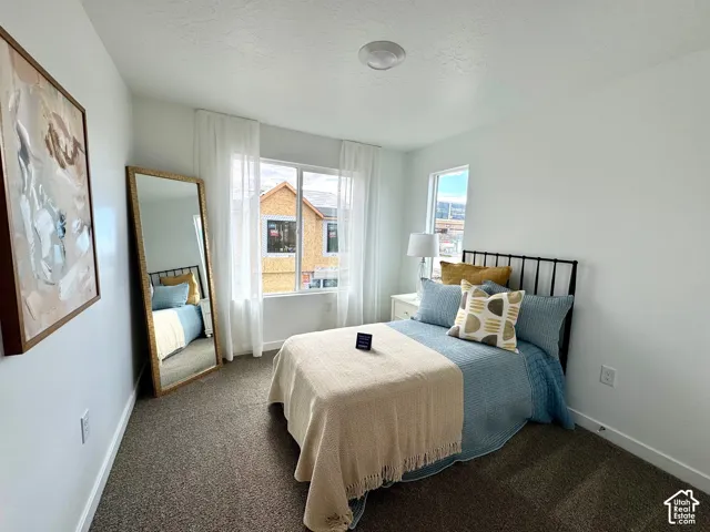 Bright room featuring a window with white drapes, white walls, and dark carpeting