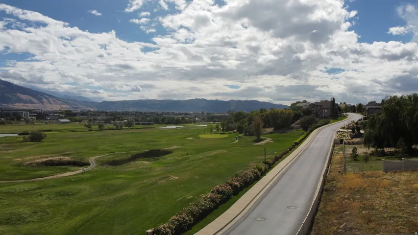 Expansive golf course frontage with a paved residential road, surrounded by established landscaping and distant mountain range