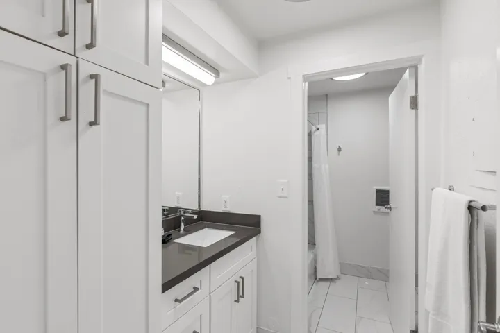 White shaker cabinetry, dark countertop, undermount sink, wall-mounted mirror, and tile flooring