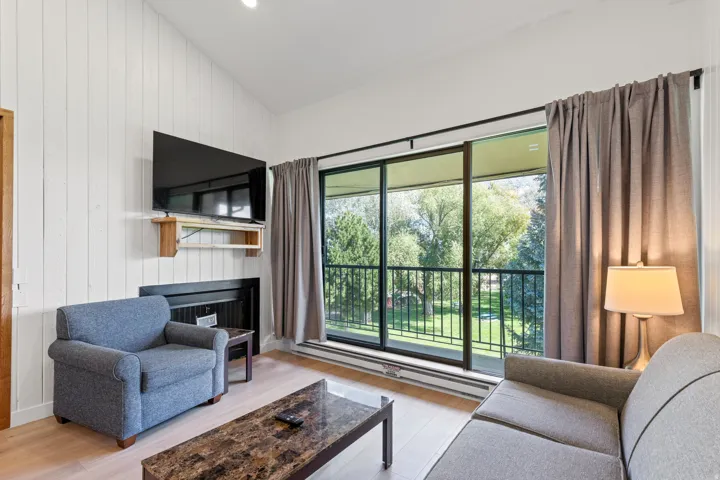 Vertical plank wall paneling, fireplace with a black surround, wood-finish flooring, sliding glass door, and a black metal balcony railing