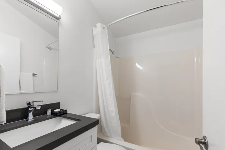Bathroom featuring a bathtub with shower, white shower curtain, vanity with an integrated sink, chrome faucet, and a wall-mounted mirror