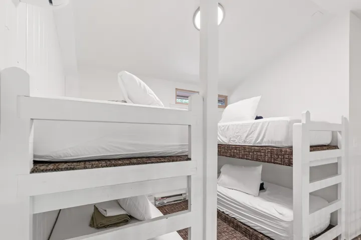 Built-in bunk beds with white frames, slatted wood-finish mattress platforms, recessed lighting, and white walls
