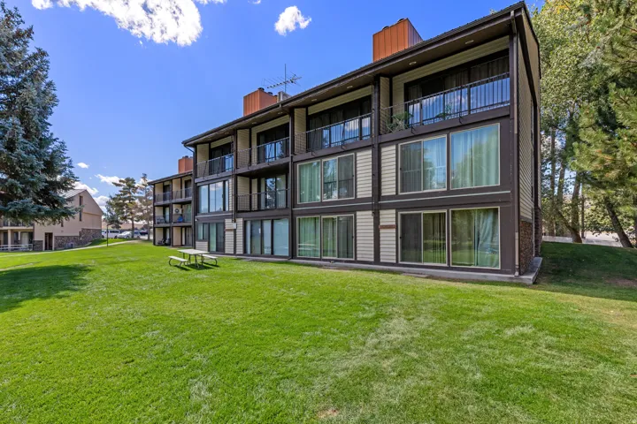 Building exterior featuring multiple levels of balconies with black railings, ground-level sliding glass doors, horizontal siding, and a surrounding green lawn