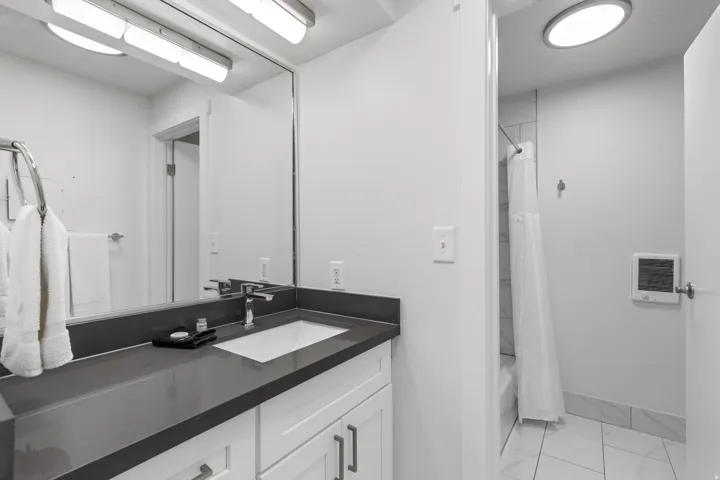 White vanity with chrome hardware, dark countertop, and integrated sink