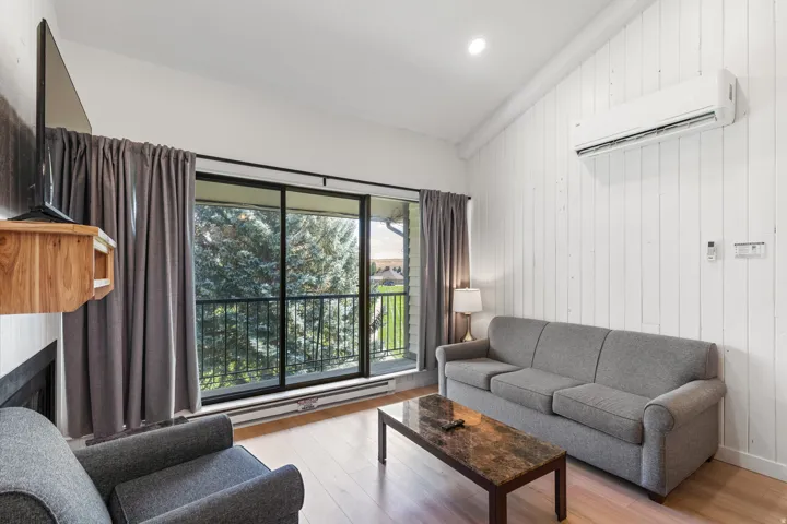 Wood-finish flooring, white paneled accent wall, vaulted ceiling, built-in wall unit, and sliding glass door to balcony