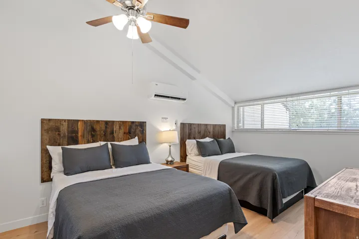 Vaulted ceiling with a ceiling fan, wall-mounted air conditioning unit, wood-finish flooring, and horizontal windows with blinds