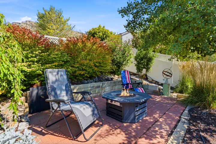 Brick paver patio featuring a fire pit, tiered landscaping, and mature plantings