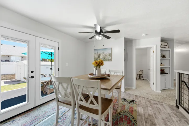 Wood-finish flooring, white French patio doors, ceiling fan with light fixture, built-in shelving unit, and painted white walls