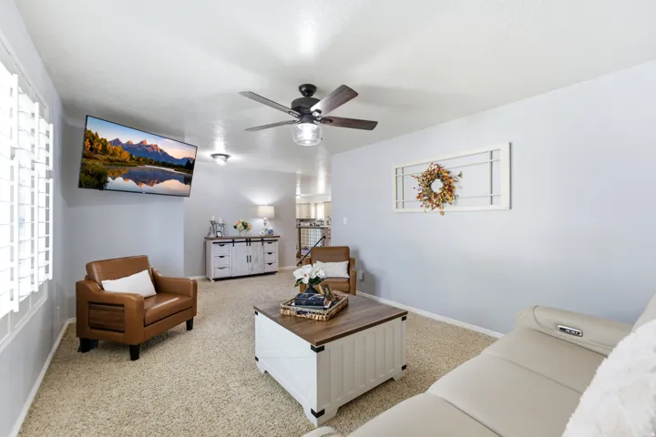 Ceiling fan with integrated lighting, recessed ceiling lights, wall-mounted television, window with plantation shutters, and textured carpeting