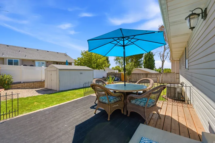 Wood deck with a black outdoor mat, fenced backyard with a green lawn, and a storage shed