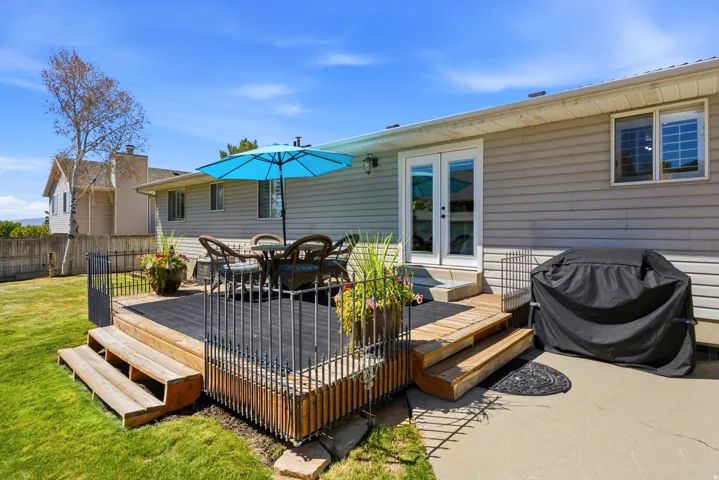 Expansive wooden deck with black metal railing, featuring steps to a concrete patio