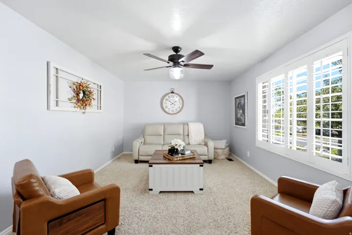 Carpeted living space featuring a ceiling fan with integrated lighting and window shutters
