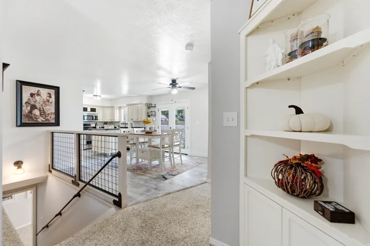 Integrated shelving unit, lower-level staircase with metal railing, wood-finish flooring, recessed lighting, and kitchen cabinetry