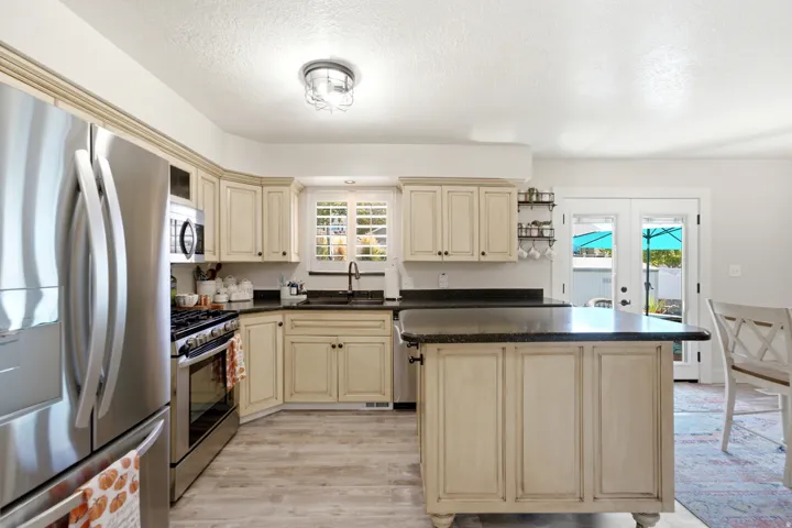 Kitchen featuring stainless steel appliances, light-toned cabinetry, dark countertops, wood-finish flooring, and French doors