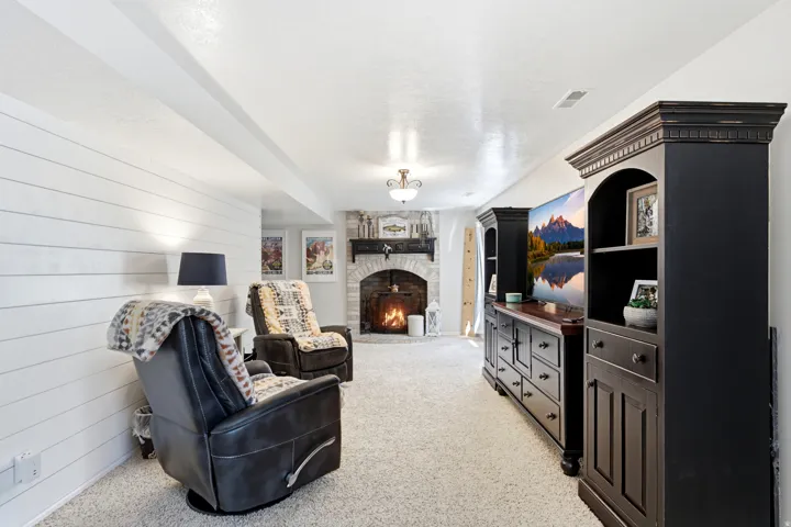 Stone-surround fireplace with hearth, white shiplap accent wall, recessed ceiling beam, and built-in entertainment cabinetry with arched details