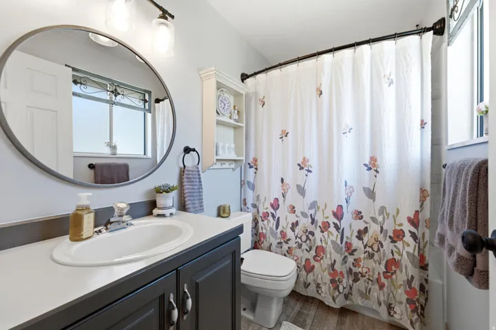 Bathroom featuring a single vanity with an integrated sink, dark cabinetry, a round mirror, and a built-in wall cabinet