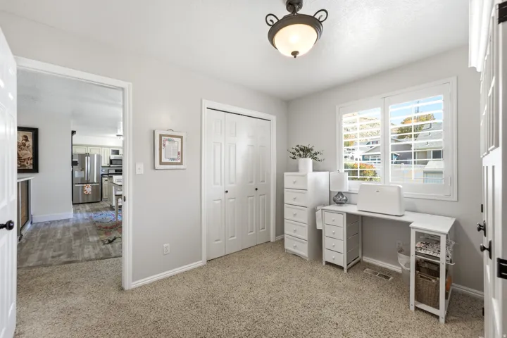 Light gray wall paint, textured carpet flooring, white bi-fold closet doors, white window shutters, and a ceiling-mounted light fixture