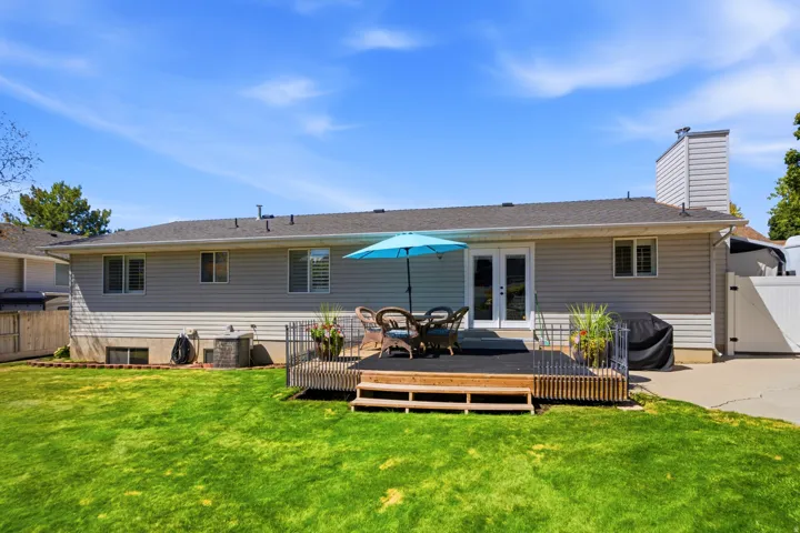 Expansive green lawn, multi-level composite deck, white double French doors, gray siding, and a white fence