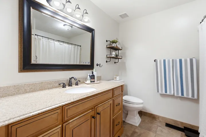 Built-in vanity with wood-finish cabinetry, a single undermount sink, a light-toned countertop, and tile flooring