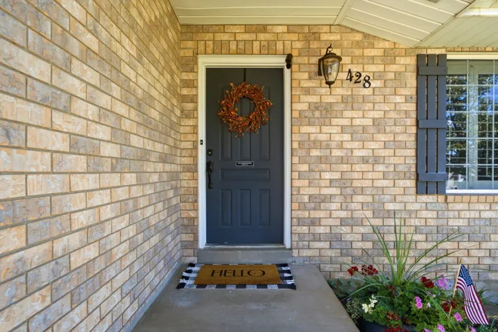 Brick exterior facade with a dark paneled door, exterior wall light fixture, and decorative window shutters