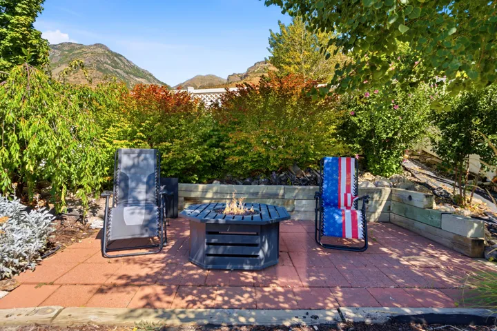 Paved patio with a fire pit, surrounded by mature trees and shrubs, with a mountain backdrop