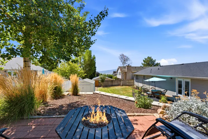Paved patio area with a built-in fire pit, mature landscaping, and an expansive lawn