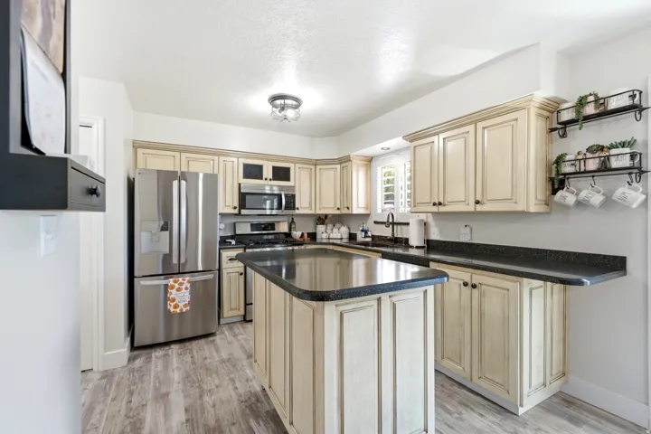 Kitchen featuring wood-finish flooring, an island with dark countertops, light-toned cabinetry, and stainless steel appliances