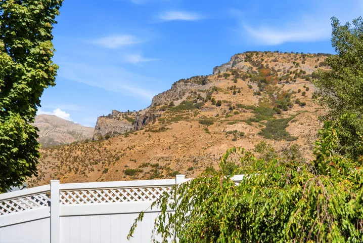 Mountainous terrain with natural vegetation, framed by a white lattice-top fence and mature trees