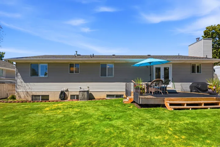 Expansive green lawn, multi-level wood deck, light gray horizontal siding, and a prominent chimney
